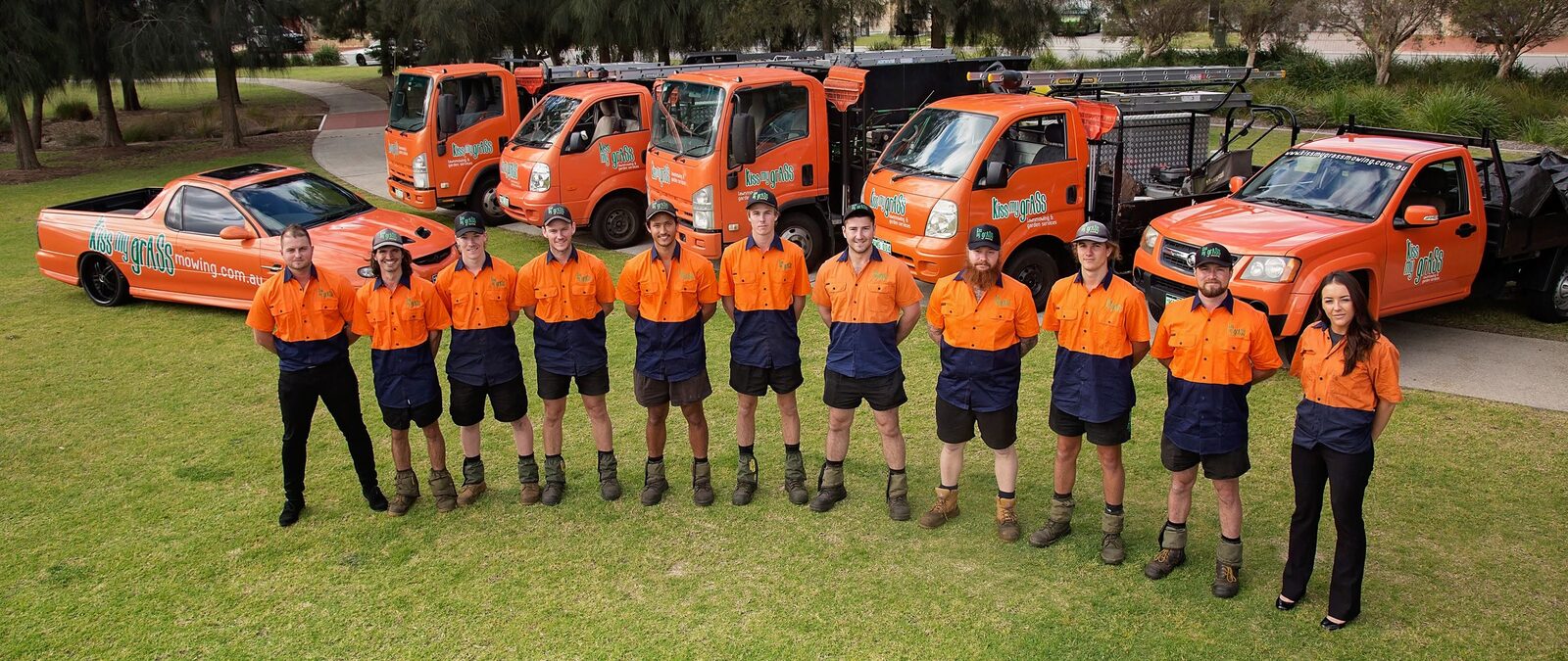 The Kiss My Grass team with their fleet of orange trucks and utes
