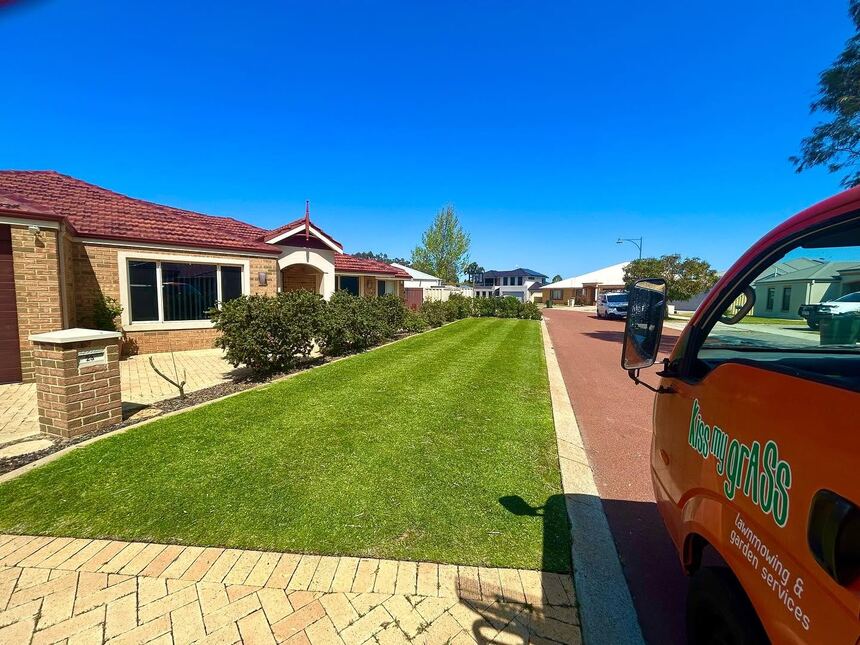The orange Kiss My Grass ute parked at the kerb beside a freshly striped verge lawn
